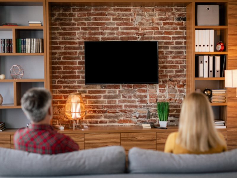 Upset mature european couple resting, watch tv with blank screen in cozy living room interior, back. Relationship problems, relax, entertainment and movie evening, bad news during covid-19 pandemic